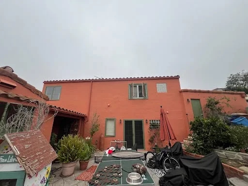 Backyard-facing wall of a Spanish-style home repainted warm coral with dark green shutters — after