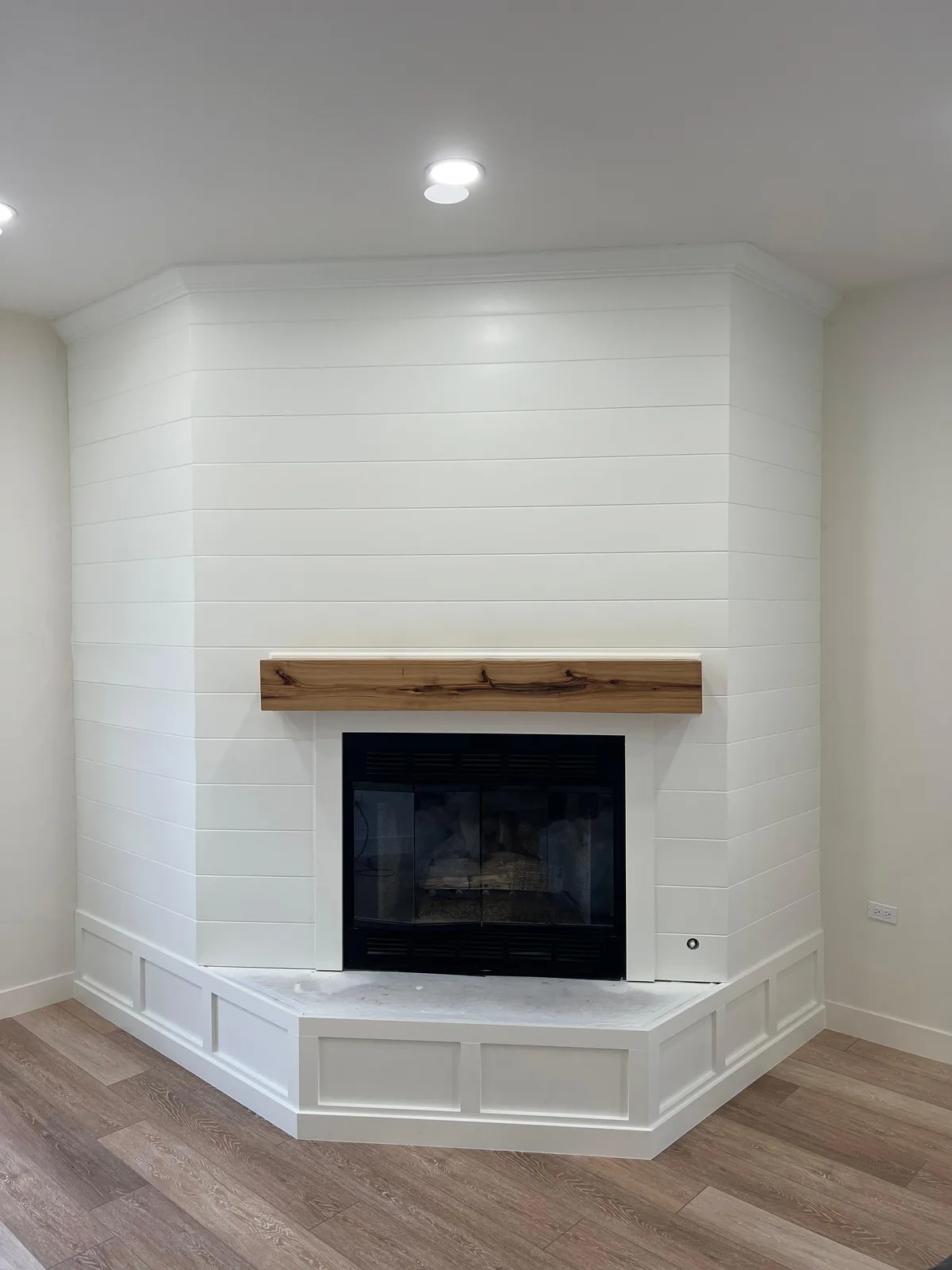 Shiplap fireplace accent wall repainted crisp white with a natural wood mantel — after