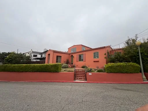 Spanish-style hillside home exterior repainted from faded stucco to warm coral — after
