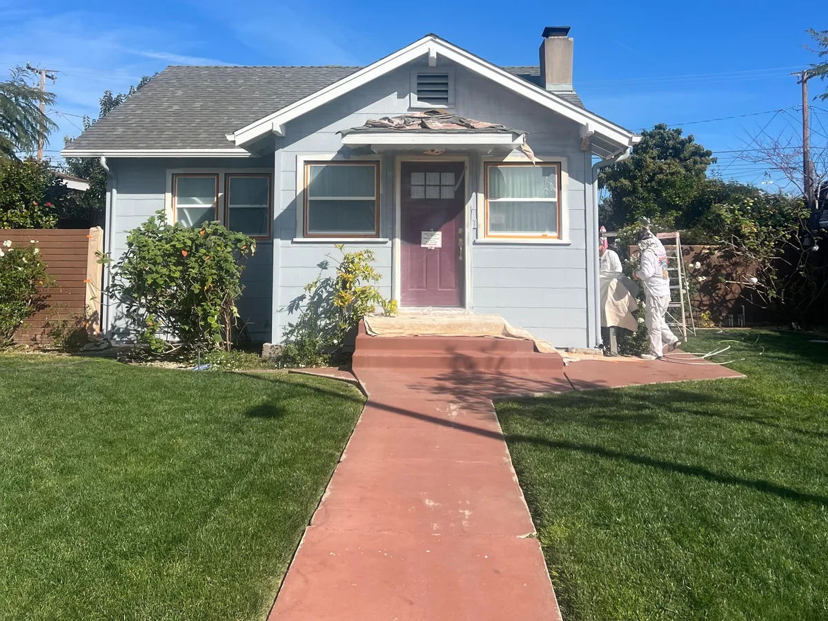 Craftsman bungalow exterior repainted light blue-gray with a new blue front door — before