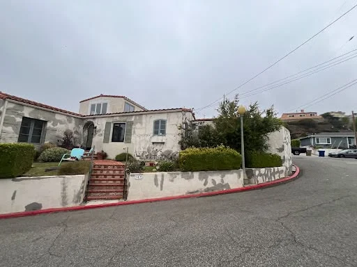 Spanish-style hillside home exterior repainted from faded stucco to warm coral — before