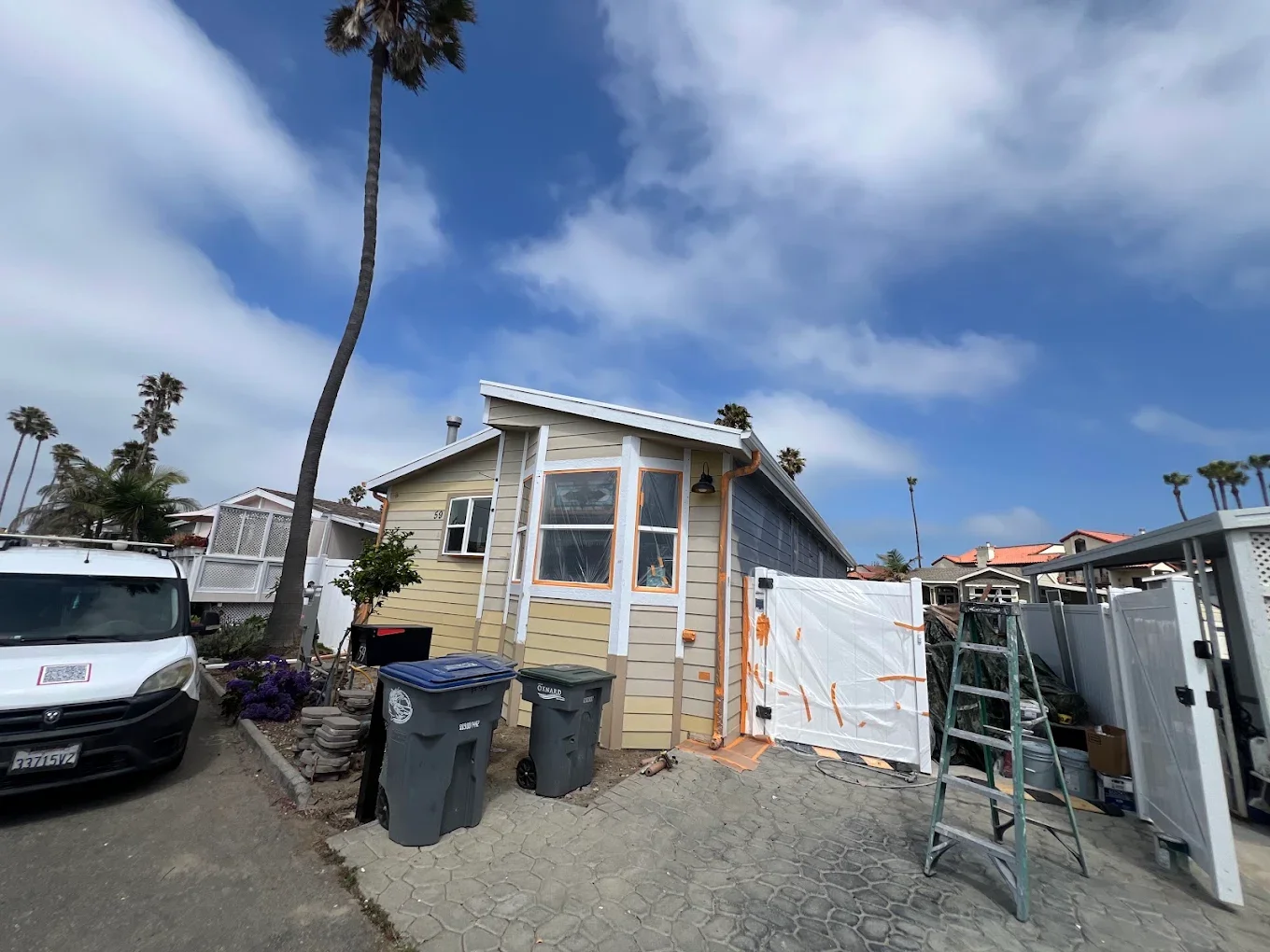 Beach mobile home exterior with tan siding, gate masked for painting