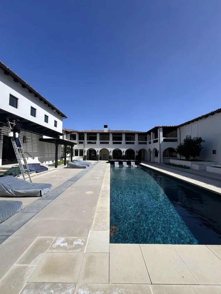 Painter on a ladder painting eaves at a Spanish-style courtyard with a lap pool